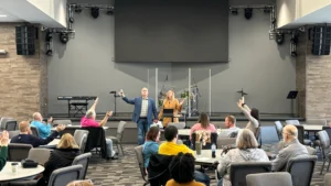 Rachel and H.K. leading a room of people in worship and prayer inside a church meeting room.